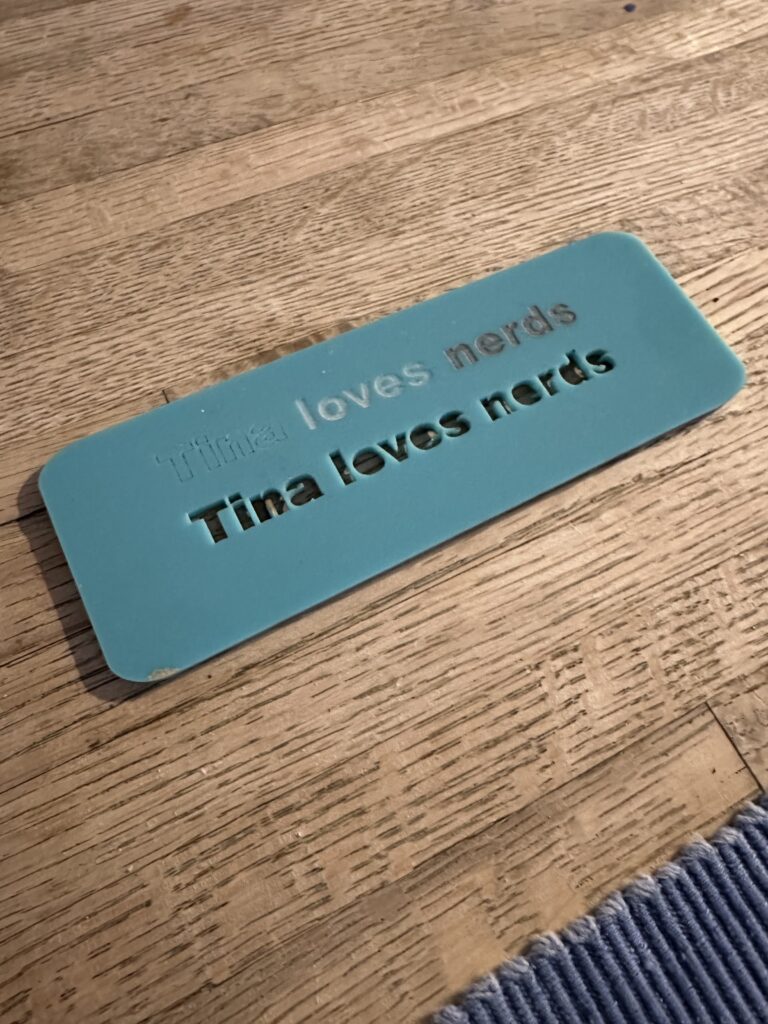 Blue scrap of acrylic with the text "Tina loves nerds" lasered through it.